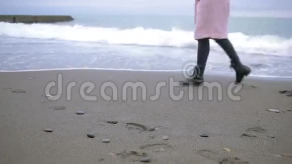 暴风雨时穿着粉红色外套的快乐女孩在海边大海在沙滩上冲刷着脚印视频的预览图