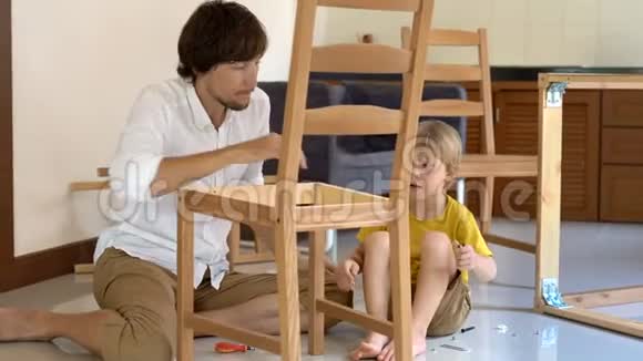 父子俩用小零件组装木制家具小男孩帮助他父亲组装一把椅子视频的预览图
