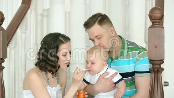 妈妈喂孩子爸爸抱着他家庭幸福妈妈爸爸和6个月大的宝宝一家人坐在楼梯上视频的预览图