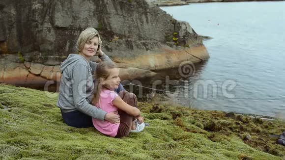 母亲和女儿坐在海边的大石头上视频的预览图
