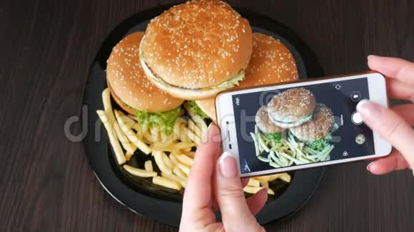 女性手在盘子上制作一个大汉堡的智能手机照片快餐图片视频的预览图