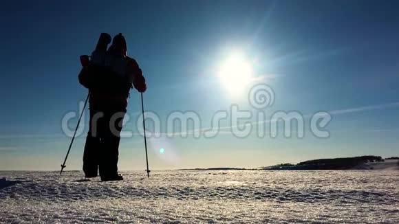 穿着雪鞋在冬天的风景中行走的人的剪影带着徒步旅行杆蓝天和视频的预览图