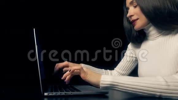 美丽的黑发女人在她的笔记本电脑上工作的黑色背景4K视频视频的预览图