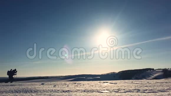 穿着雪鞋在冬天的风景中行走的人的剪影带着徒步旅行杆蓝天和视频的预览图