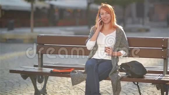 一个红发美女坐在街上的长凳上用手机聊天视频的预览图