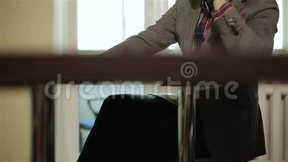 那个穿格子夹克的商人正坐在窗户前的桌子旁的手机上聊天视频的预览图
