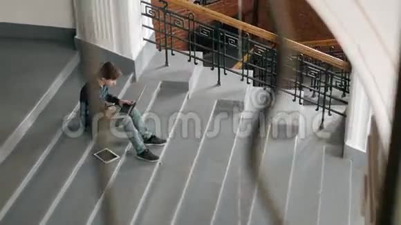 自由职业和技术英俊的年轻人在现代阁楼办公室里坐在室内的楼梯上用笔记本电脑工作视频的预览图