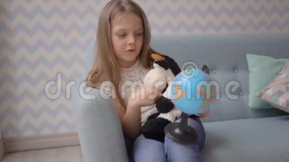 可爱的女孩在家里坐在沙发上拿着一个小地球仪旋转着视频的预览图