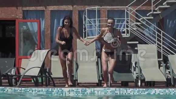 快乐的女朋友跑着跳进游泳池举起水滴慢动作视频的预览图