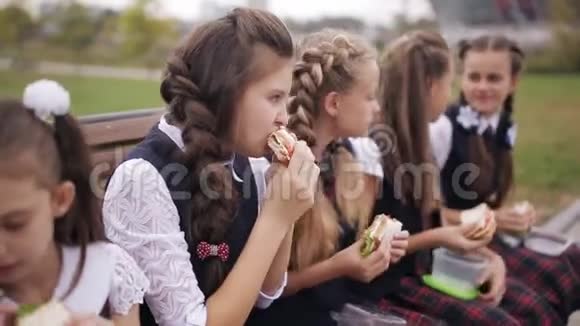 女大学生穿着相同的校服在公园休息时吃三明治微笑视频的预览图