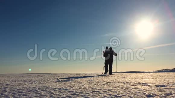 穿着雪鞋在冬天的风景中行走的人的剪影带着徒步旅行杆蓝天和视频的预览图