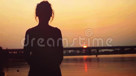 美丽的女人站在沙滩上的剪影看着太阳在日落时缓慢地下山1920x1080视频的预览图