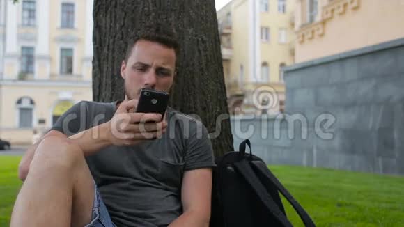 男子在公园里坐在树下通过互联网使用智能手机购物时使用信用卡视频的预览图