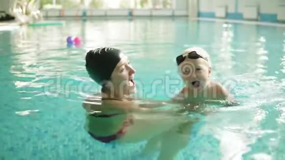 快乐的小男孩和他的母亲一起在游泳池里游泳她抱着他教游泳快乐视频的预览图
