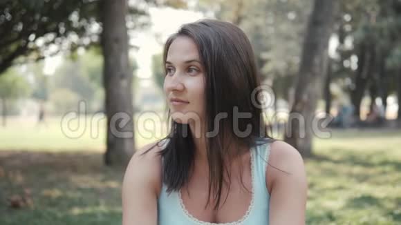 阳光明媚的夏日美丽的年轻女子坐在公园草坪上的画像视频的预览图