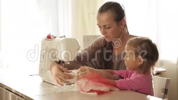 年轻漂亮的母亲和她可爱的小女儿一起在缝纫机上工作视频的预览图