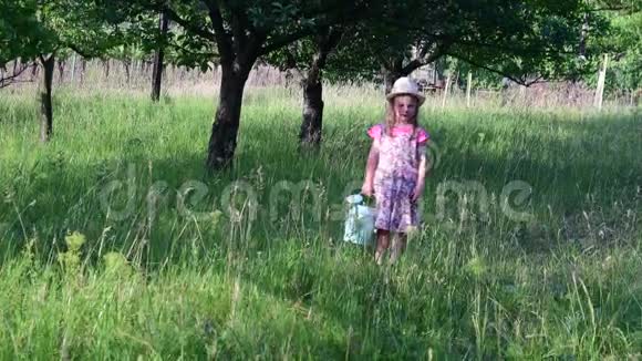 小女孩穿花裙和白帽子小女孩在自然花园里拿着水罐视频的预览图
