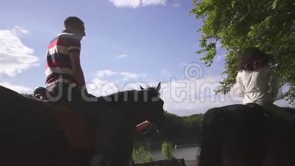 幸福的年轻家庭夫妇在湖边的绿色公园骑马蓝天背景视频的预览图