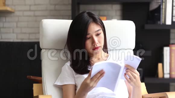 美丽的肖像年轻的亚洲女人放松坐在客厅看书在家女孩学习文学视频的预览图