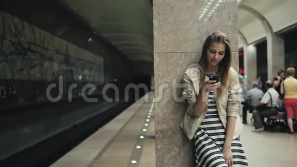 在火车站带智能手机的女孩一位年轻的白种人妇女的肖像在等待着视频的预览图