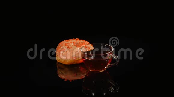 杯茶和带有橙色釉的甜甜圈在黑色背景上旋转视频的预览图