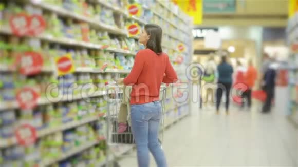 美丽的女人带着女儿在超市购物年轻的母亲在市场上为孩子选择食物视频的预览图