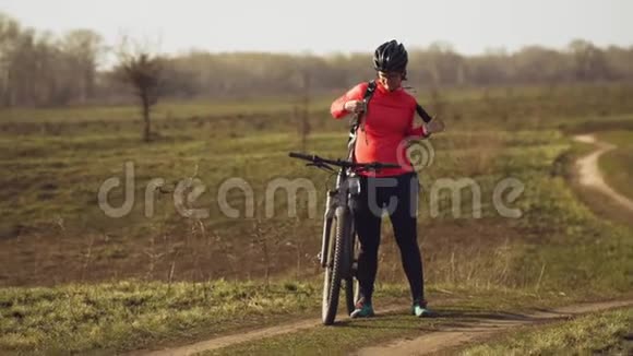 运动白种人女人吃蛋白吧骑山上的自行车自然女运动员戴头盔休息视频的预览图