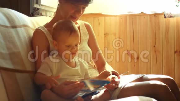 妈妈和她两岁的小男孩坐在阳光明媚的房间里的扶手椅上看书视频的预览图