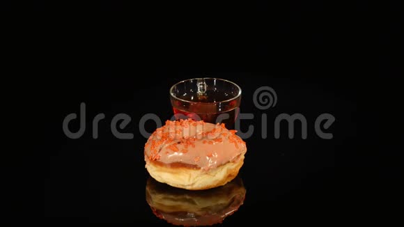杯茶和带有橙色釉的甜甜圈在黑色背景上旋转视频的预览图