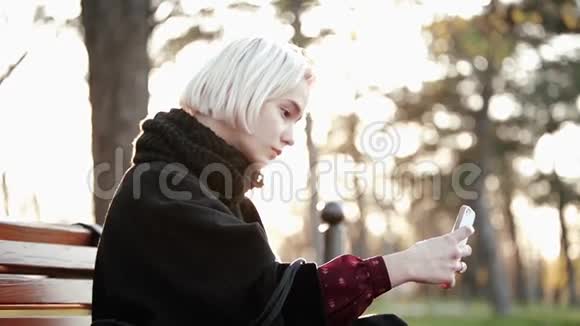 外面的金发女孩拿着智能手机咖啡自拍一张严肃漂亮的脸阳光闪烁视频的预览图