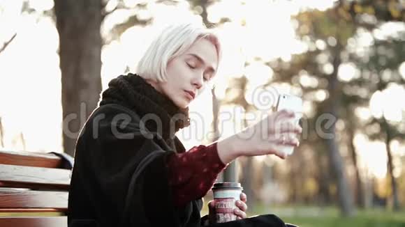 外面的金发女孩拿着智能手机咖啡自拍一张严肃漂亮的脸阳光闪烁视频的预览图