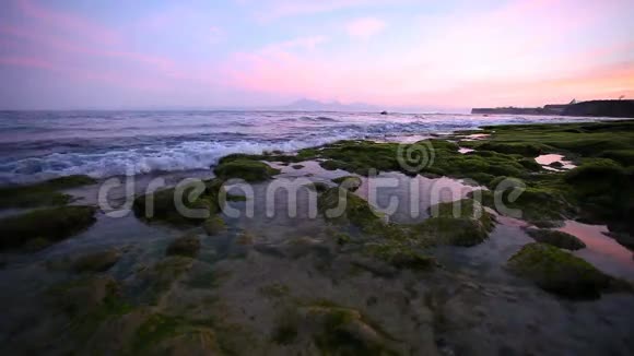 日出时平静的海洋小波浪冲刷海滩上的岩石背景是山脉视频的预览图