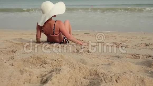 穿比基尼戴太阳帽的女人在海边晒日光浴的后景视频的预览图