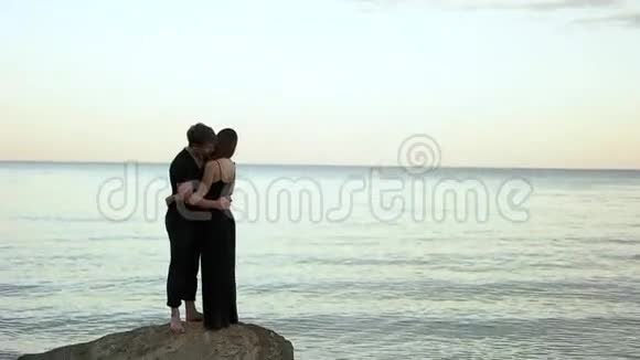 穿着黑色衣服拥抱在海边岩石上的夫妇视频的预览图