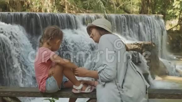 一位年轻的母亲和她可爱的女儿靠着瀑布休息视频的预览图