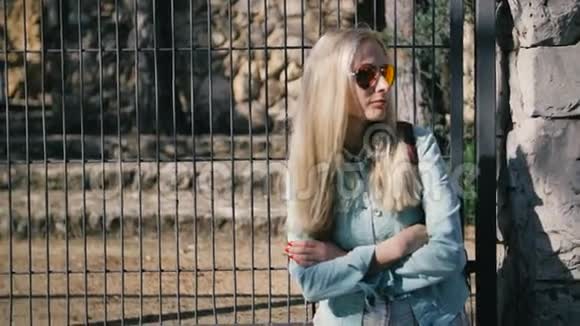 孤独的年轻女孩穿着夹克和太阳镜在公共汽车站等待交通视频的预览图