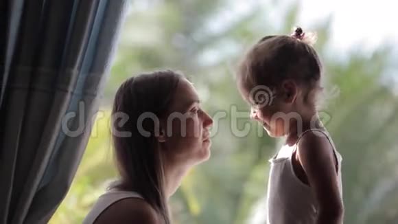 妈妈和可爱的小女儿在窗台上说话微笑着拥抱视频的预览图