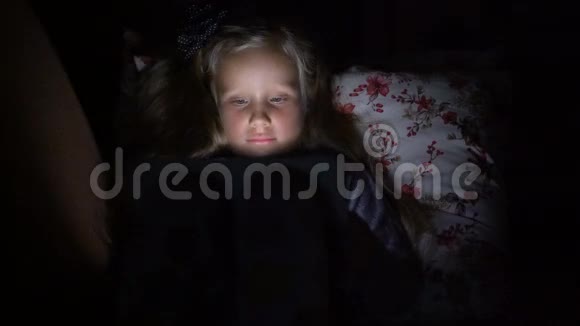 一个五岁的女孩躺在黑暗的沙发上看着卡通视频的预览图