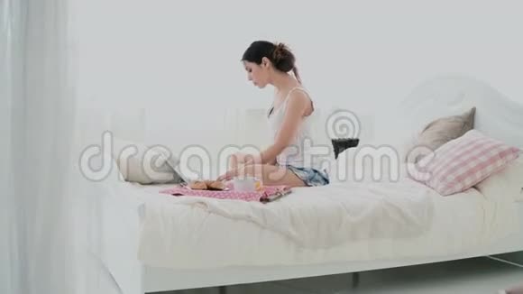 年轻的黑发女人躺在床上漂亮的女孩在早餐时使用笔记本电脑喝果汁跳舞视频的预览图