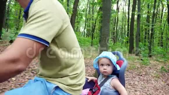 一个男人带着一个孩子在森林里骑自行车夏天孩子坐在一张特殊的椅子上视频的预览图