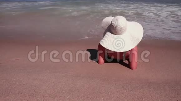 穿着比基尼和白色太阳帽的女性在海沙天堂海滩上日光浴的后景视频的预览图