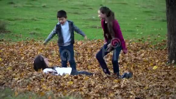 妈妈和她的孩子们正在秋天的森林里玩得很开心他们跳起来把树叶扔到空中他们是视频的预览图