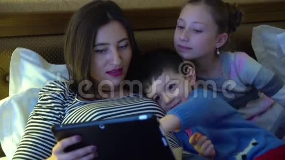 一位年轻的母亲两个孩子躺在旅馆的床上通过平板电脑使用互联网他们很开心视频的预览图