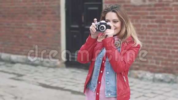 女孩在电影摄影机上给她的朋友拍照穿红色夹克的金发美女拍照微笑视频的预览图