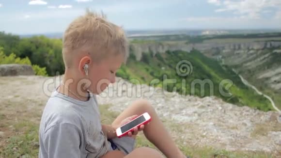 在山区背景下小男孩用智能手机听音乐视频的预览图