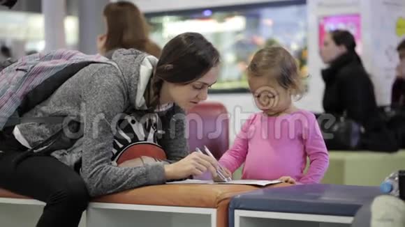 母亲和女儿坐在机场候机大厅拿着练习本视频的预览图