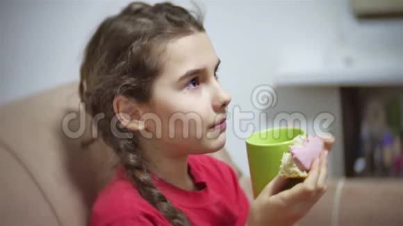 少女吃三明治喝茶看电视女孩在室内吃三明治视频的预览图