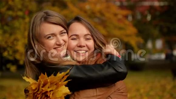 美丽的少女在秋天的公园里玩两个欢笑的小女孩在秋天公园拥抱抱着一个视频的预览图