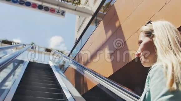 在露天商场的自动扶梯上移动的年轻女子视频的预览图