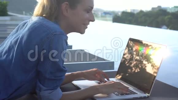 美丽的金发女人在笔记本电脑上工作躺在阳光下男人在无限游泳池的背景下游泳视频的预览图